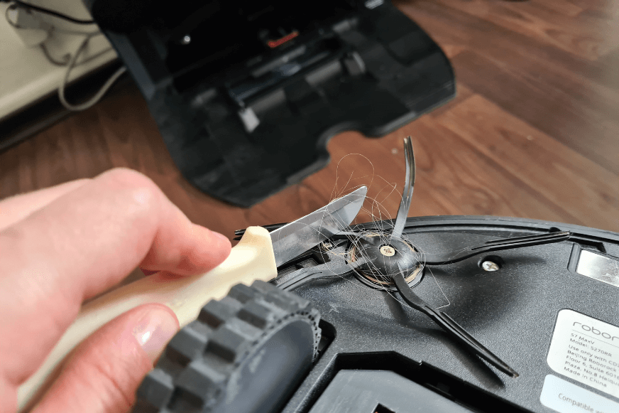 Haare werden von der Seitenbürste des Roborock S7 MaxV Ultra mit Hilfe eines Messers entfernt